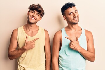 Young gay couple wearing casual clothes cheerful with a smile of face pointing with hand and finger up to the side with happy and natural expression on face