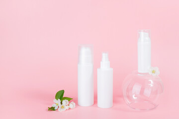 Set of cosmetic for skin care face, body. White blank cosmetics bottles and tube on glass podium and flowering branch, pink background. Natural Organic Spa Cosmetic Beauty Concept Mockup