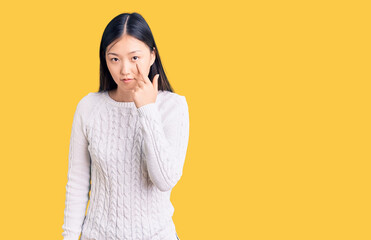 Young beautiful chinese woman wearing casual sweater pointing to the eye watching you gesture, suspicious expression