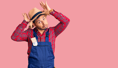 Handsome latin american young man weaing handyman uniform doing bunny ears gesture with hands palms looking cynical and skeptical. easter rabbit concept.