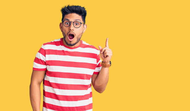 Handsome latin american young man wearing casual clothes and glasses surprised pointing with finger to the side, open mouth amazed expression.