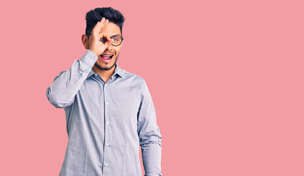 Handsome latin american young man wearing business clothes and glasses smiling happy doing ok sign with hand on eye looking through fingers