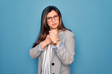 Young hispanic business woman wearing glasses standing over blue isolated background Ready to fight with fist defense gesture, angry and upset face, afraid of problem