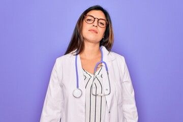 Professional doctor woman wearing stethoscope and medical coat over purple background Relaxed with serious expression on face. Simple and natural looking at the camera.