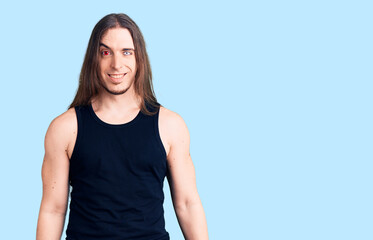 Young adult man with long hair wearing rocker style with black clothes and contact lenses looking...