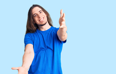 Young adult man with long hair wearing swimwear looking at the camera smiling with open arms for hug. cheerful expression embracing happiness.