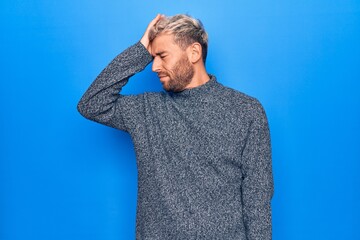 Young handsome blond man wearing casual sweater standing over isolated blue background surprised...