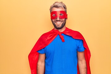 Handsome blond man wearing super hero costume with mask and cape over yellow background with a...