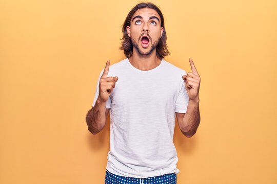 Young handsome man wearing casual clothes amazed and surprised looking up and pointing with fingers and raised arms.