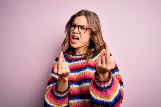Young beautiful blonde girl wearing glasses and casual sweater over pink isolated background Showing middle finger doing fuck you bad expression, provocation and rude attitude. Screaming excited