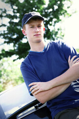 A boy with cap leaning against a car