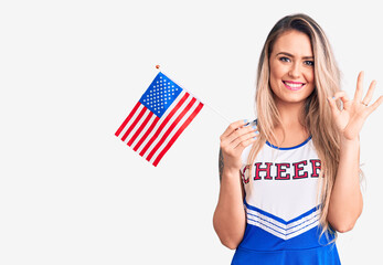 Young beautiful blonde woman wearing cheerleader uniform holding united states flag doing ok sign...