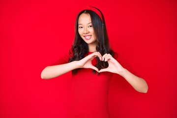 Young beautiful chinese girl wearing casual clothes smiling in love doing heart symbol shape with hands. romantic concept.