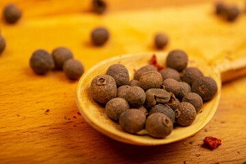 Black allspice peas in a wooden spoon on a wooden background. Close up.