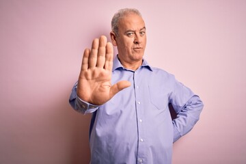 Middle age handsome hoary man wearing casual shirt standing over pink background doing stop sing with palm of the hand. Warning expression with negative and serious gesture on the face.