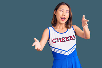 Young beautiful chinese girl wearing cheerleader uniform smiling cheerful offering hands giving...
