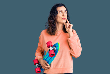 Young beautiful hispanic woman holding skate serious face thinking about question with hand on chin, thoughtful about confusing idea