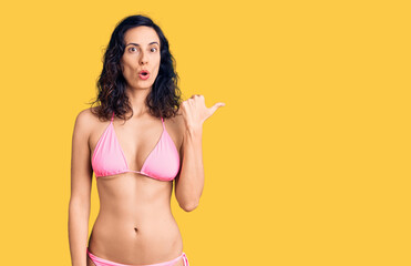 Young beautiful hispanic woman wearing bikini surprised pointing with hand finger to the side, open mouth amazed expression.