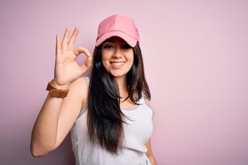 Naklejka premium Young brunette woman wearing casual sport cap over pink background smiling positive doing ok sign with hand and fingers. Successful expression.