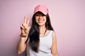 Obraz na płótnie Canvas Young brunette woman wearing casual sport cap over pink background showing and pointing up with fingers number two while smiling confident and happy.