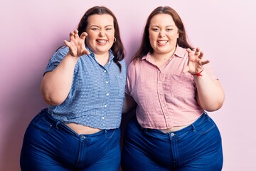 Young plus size twins wearing casual clothes smiling funny doing claw gesture as cat, aggressive...