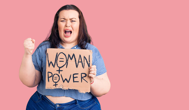 Young plus size woman holding woman power banner annoyed and frustrated shouting with anger, yelling crazy with anger and hand raised