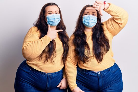 Young plus size twins wearing medical mask smiling making frame with hands and fingers with happy face. creativity and photography concept.