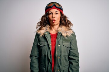 Middle age skier woman wearing snow sportswear and ski goggles over white background making fish face with lips, crazy and comical gesture. Funny expression.