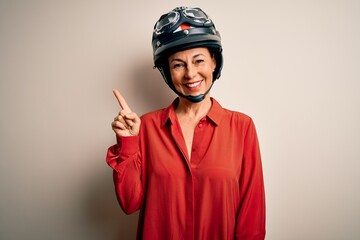 Middle age motorcyclist woman wearing motorcycle helmet over isolated white background with a big smile on face, pointing with hand and finger to the side looking at the camera.