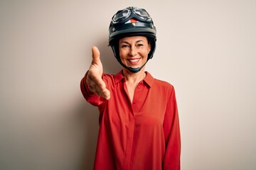 Middle age motorcyclist woman wearing motorcycle helmet over isolated white background smiling friendly offering handshake as greeting and welcoming. Successful business.