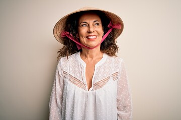 Middle age brunette woman wearing asian traditional conical hat over white background looking away to side with smile on face, natural expression. Laughing confident.