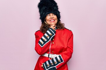 Middle age beautiful wales guard woman wearing traditional uniform over pink background with hand on chin thinking about question, pensive expression. Smiling with thoughtful face. Doubt concept.