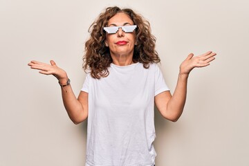 Middle age beautiful woman wearing funny thug life sunglasses over white background clueless and...