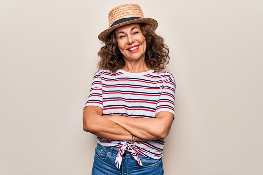 Middle age beautiful woman wearing striped t-shirt and hat over isolated white background happy face smiling with crossed arms looking at the camera. Positive person.