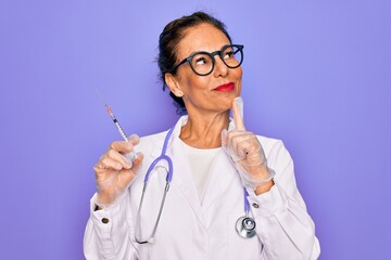 Middle age senior professional doctor woman holding syringe with medical vaccine serious face...