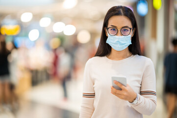 Asian woman wearing face mask And hold a mobile phone shopping in department store during corona...