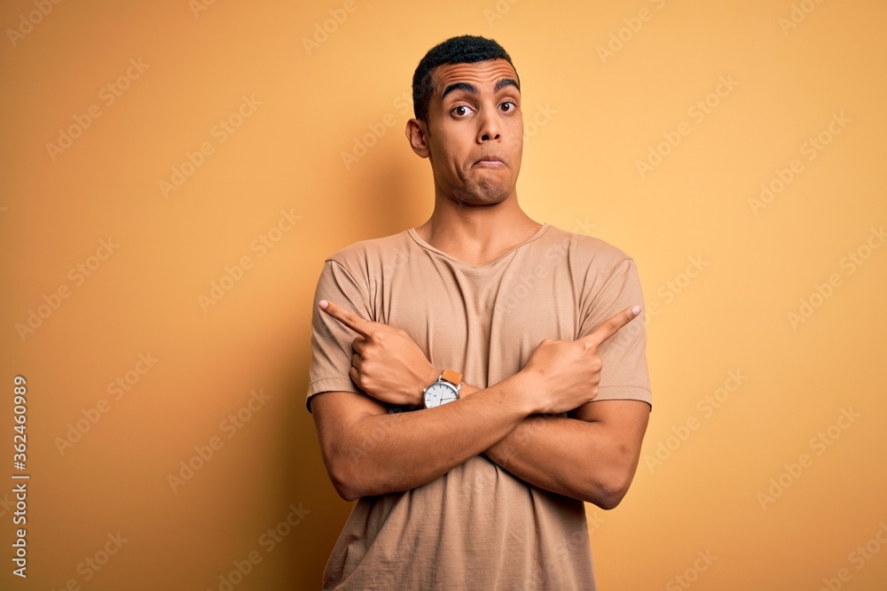 Wall mural young handsome african american man wearing casual t-shirt standing over yellow background pointing 