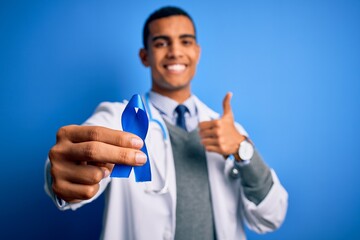 Young handsome african american doctor man holding blue cancer ribbon symbol happy with big smile...