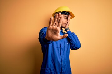 Young handsome african american worker man wearing blue uniform and security helmet covering eyes...