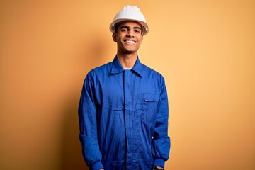 Young handsome african american worker man wearing blue uniform and security helmet with a happy...