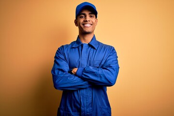 Young african american mechanic man wearing blue uniform and cap over yellow background happy face...
