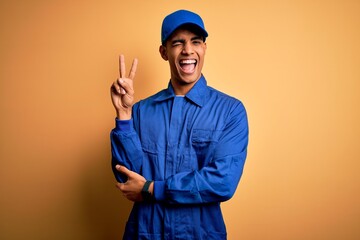 Young african american mechanic man wearing blue uniform and cap over yellow background smiling...