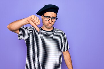 Handsome man with blue eyes wearing striped t-shirt and french beret over purple background looking unhappy and angry showing rejection and negative with thumbs down gesture. Bad expression.