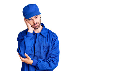 Young hispanic man wearing painter uniform thinking looking tired and bored with depression problems with crossed arms.