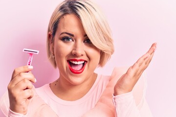 Young beautiful blonde plus size woman holding depilation razor over isolated pink background celebrating achievement with happy smile and winner expression with raised hand