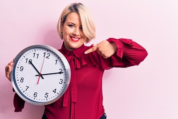 Young beautiful blonde plus size woman doing countdown using big clock over pink background smiling happy pointing with hand and finger