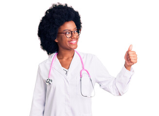 Young african american woman wearing doctor coat and stethoscope looking proud, smiling doing thumbs up gesture to the side