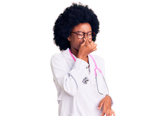 Young african american woman wearing doctor coat and stethoscope smelling something stinky and disgusting, intolerable smell, holding breath with fingers on nose. bad smell