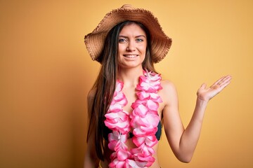 Young beautiful woman with blue eyes on vacation wearing bikini and hawaiian lei smiling cheerful presenting and pointing with palm of hand looking at the camera.