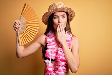 Young beautiful woman with blue eyes on vacation wearing bikini holding hand fan cover mouth with hand shocked with shame for mistake, expression of fear, scared in silence, secret concept